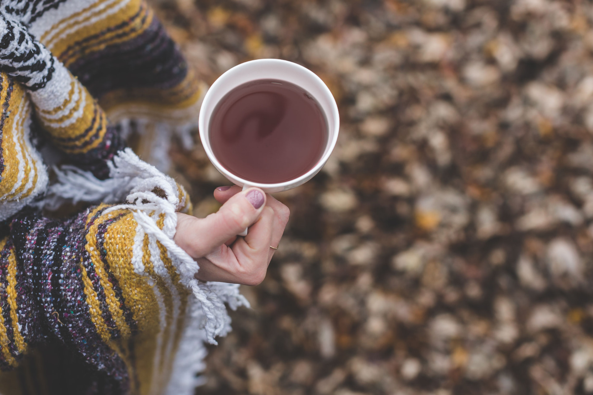Hands wrapped in a cozy blanket holding a warm cup of tea outdoors